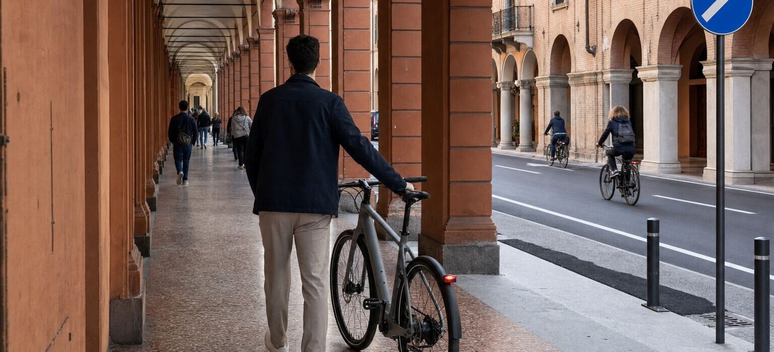Una bicicletta condotta a mano sotto un lungo portico di mattoni con archi in una città del nord Italia
